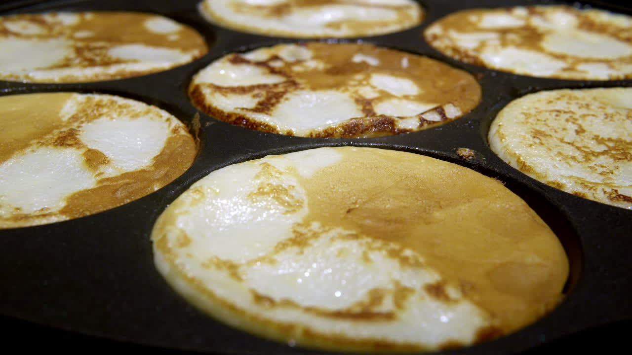 Frying Swedish mini pancakes called plättar, in a black frying pan. Home cooking concept.
