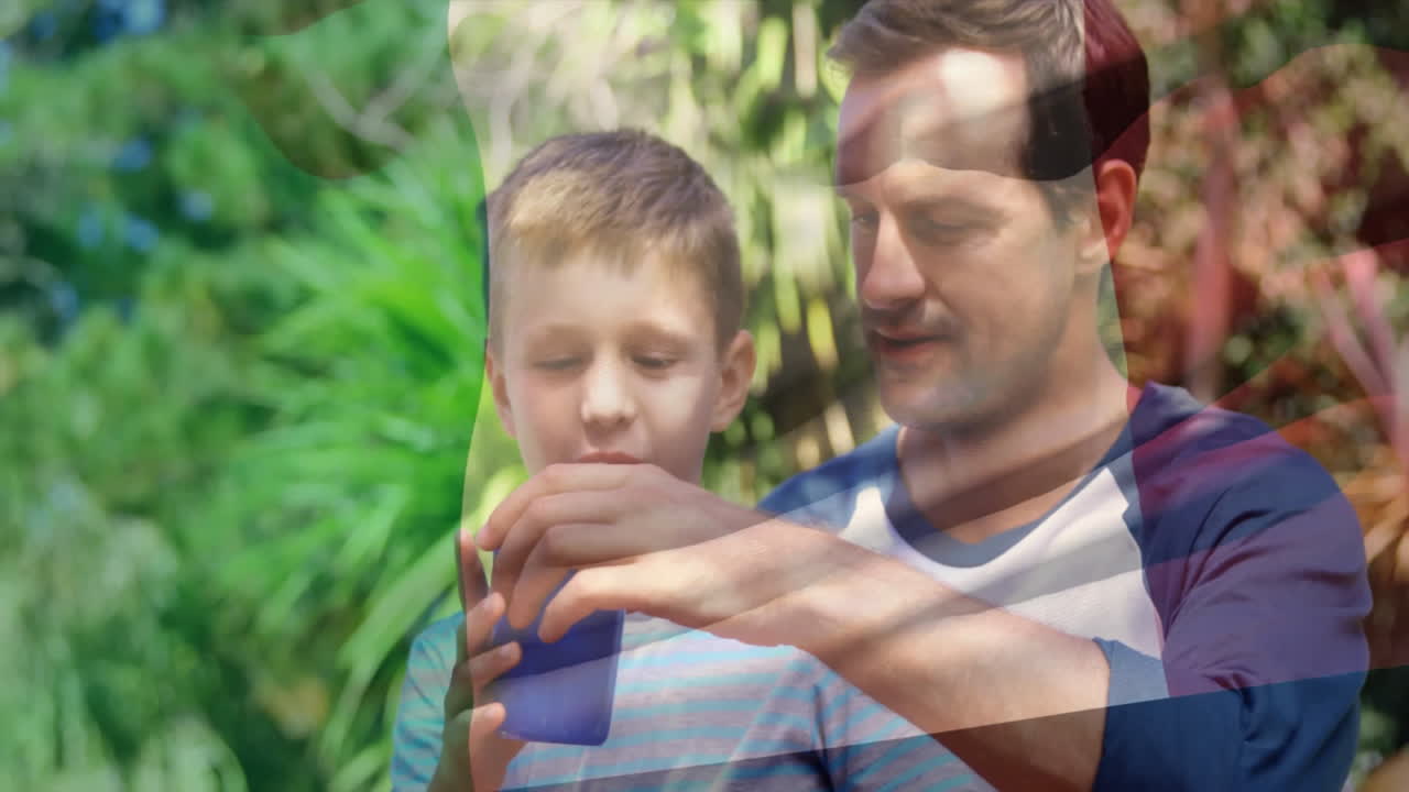In giardino, padre che aiuta il bambino a bere da una tazza blu sotto un cielo soleggiato.