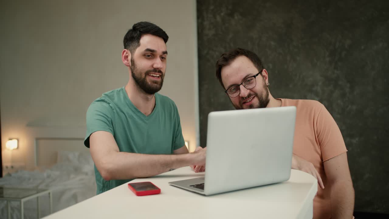 pareja gay feliz relajarse divertirse usando tecnología viendo películas en internet juntos mientras se sientan a la mesa