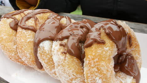 Close-Up-Pouring-chocolate-sauce-on-sugared-donuts