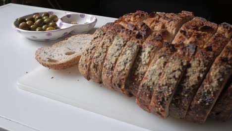 freshly sliced olive bread on a white chopping board with a side of green olives