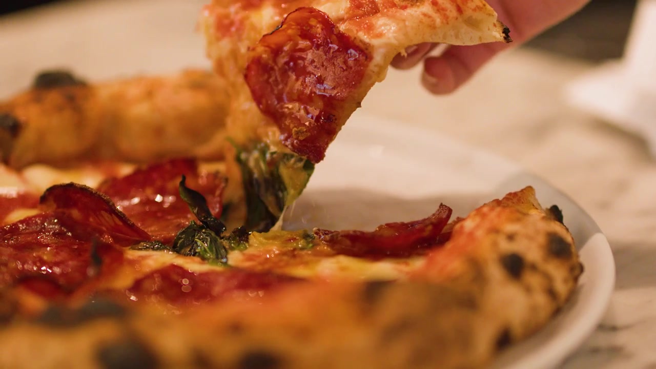 Mano che solleva una fetta di pizza fresca al salame piccante.
