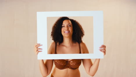 studio shot of confident natural woman in underwear making funny faces in picture frame