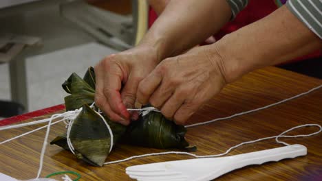 string being hand tied onto rice triangle wrapped in leaf placed on table top