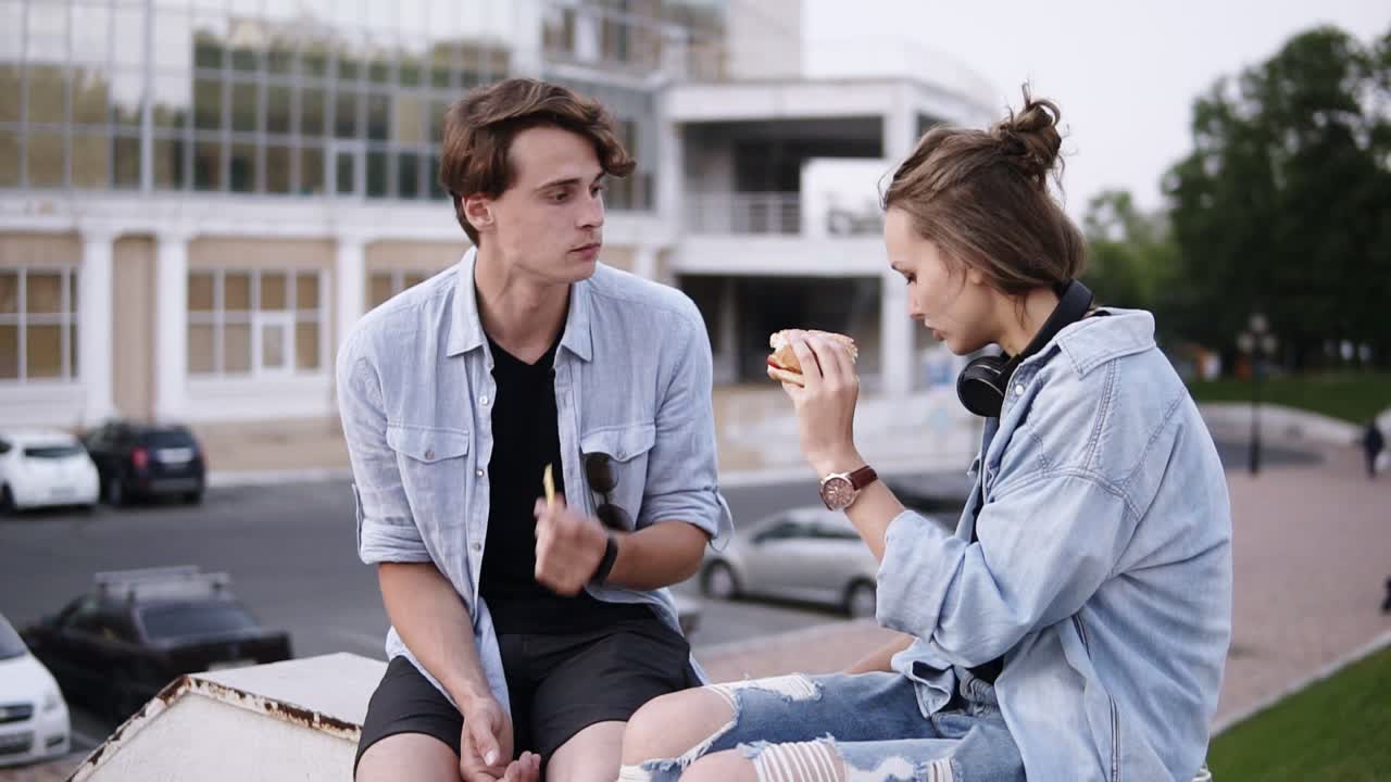 공원의 벽돌 위에 앉아 패스트푸드, 햄버거, 감자 ⁇ 김을 먹고 함께 시간을 보내는 두 친구의 클로즈업