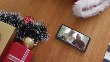 padre y hijo biraciales sonrientes con sombreros de santa en una videollamada de navidad en un teléfono inteligente