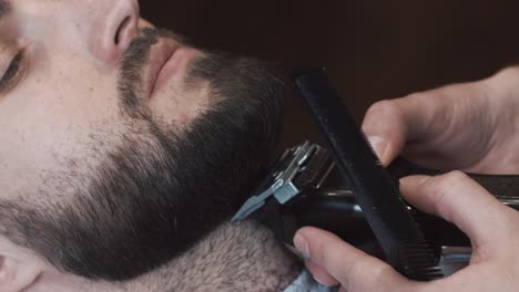 barber trimming a man's beard with electric clippers