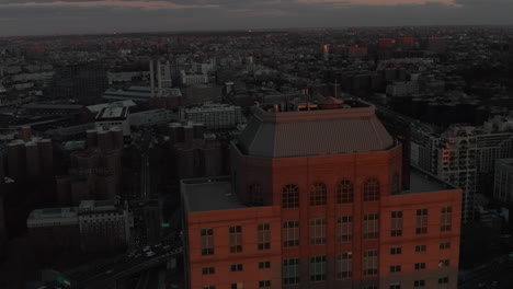 Forwards-fly-over-high-rise-apartment-building-with-top-illuminated-by-last-sun-rays.-Urban-neighbourhood-at-dusk.-Brooklyn,-New-York-City,-USA