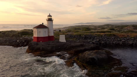 coquille river lighthouse against sunset sky with splashing waves on rocky shoreline in bandon, oregon