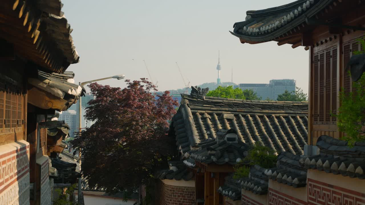 A view moving left along a traditional street in Bukchon Hanok Village, Seoul, reveals sunset sunlit Hanok houses and a distant cityscape featuring the iconic N Seoul Tower, Truck Left