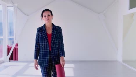 confident woman holding a yoga mat in a stylish suit, embodying strength and elegance in a bright, modern studio environment