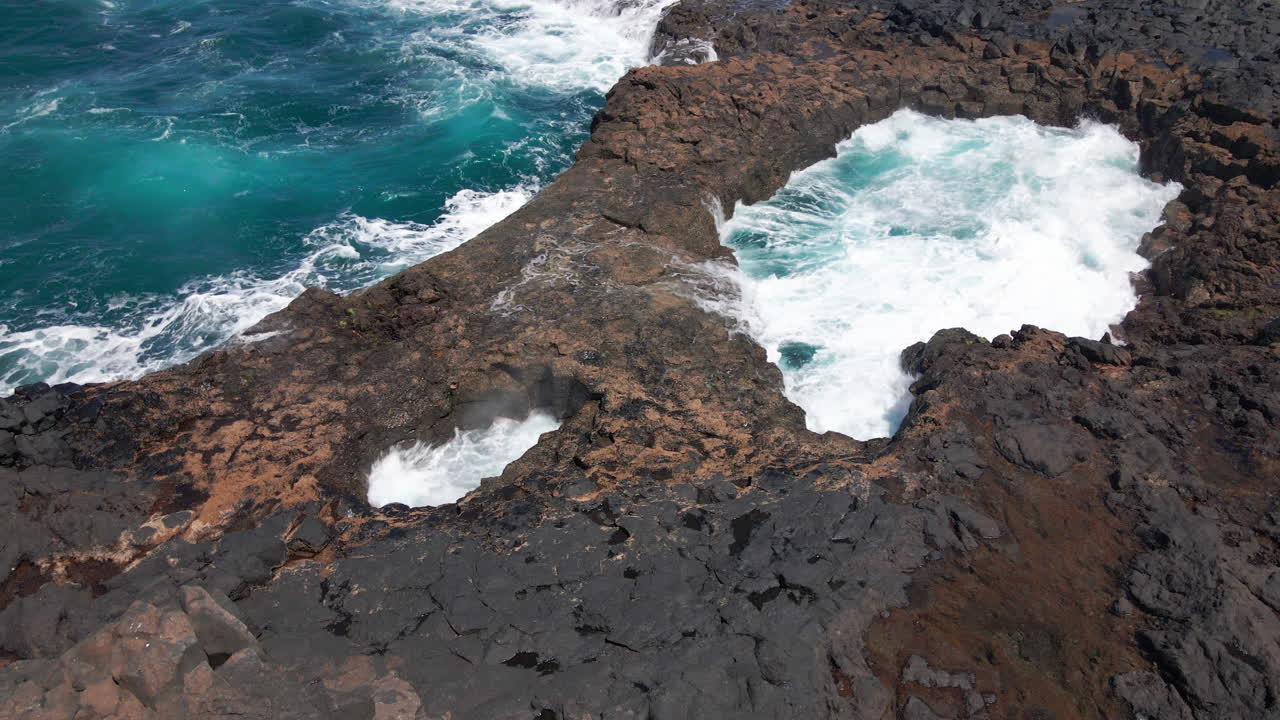 전경에 있는 바다 위의 드론 탑샷 정적은 그란 카나리아의 돌 해변 위로 그란 카나리아 바다 절벽 파도가 흐릅니다.