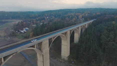 vista aérea del camión blanco que se mueve en el puente sobre el río en el oscuro día de otoño, disparo de drones
