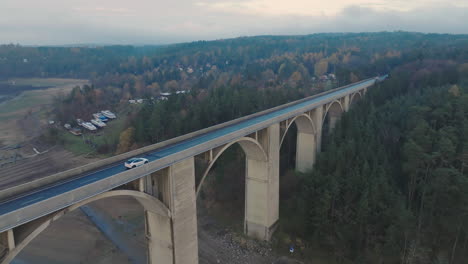 aerial view of white car moving on bridge above river on dark autumn day, drone shot