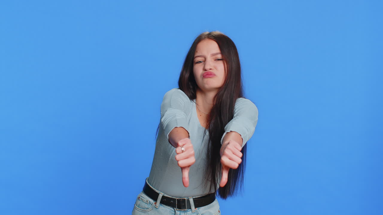 Upset attractive young woman girl showing thumbs down sign gesture disapproval dissatisfied dislike