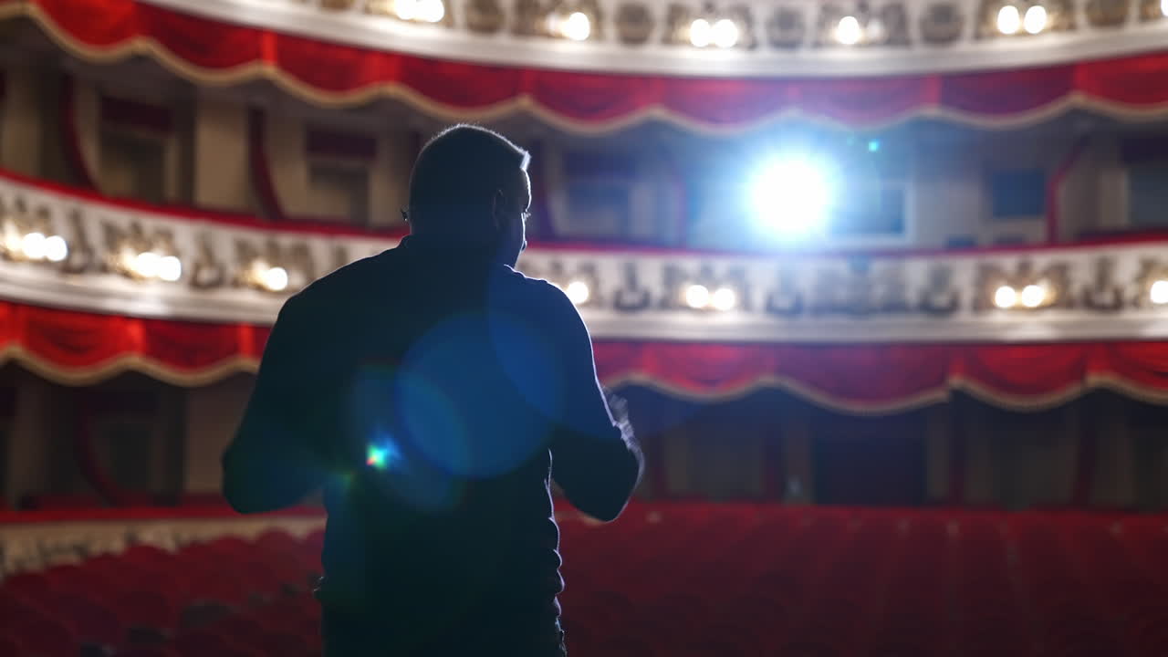 Speaker on stage against bright spotlight. Back view of an actor man during the rehearsal in the classical theater.