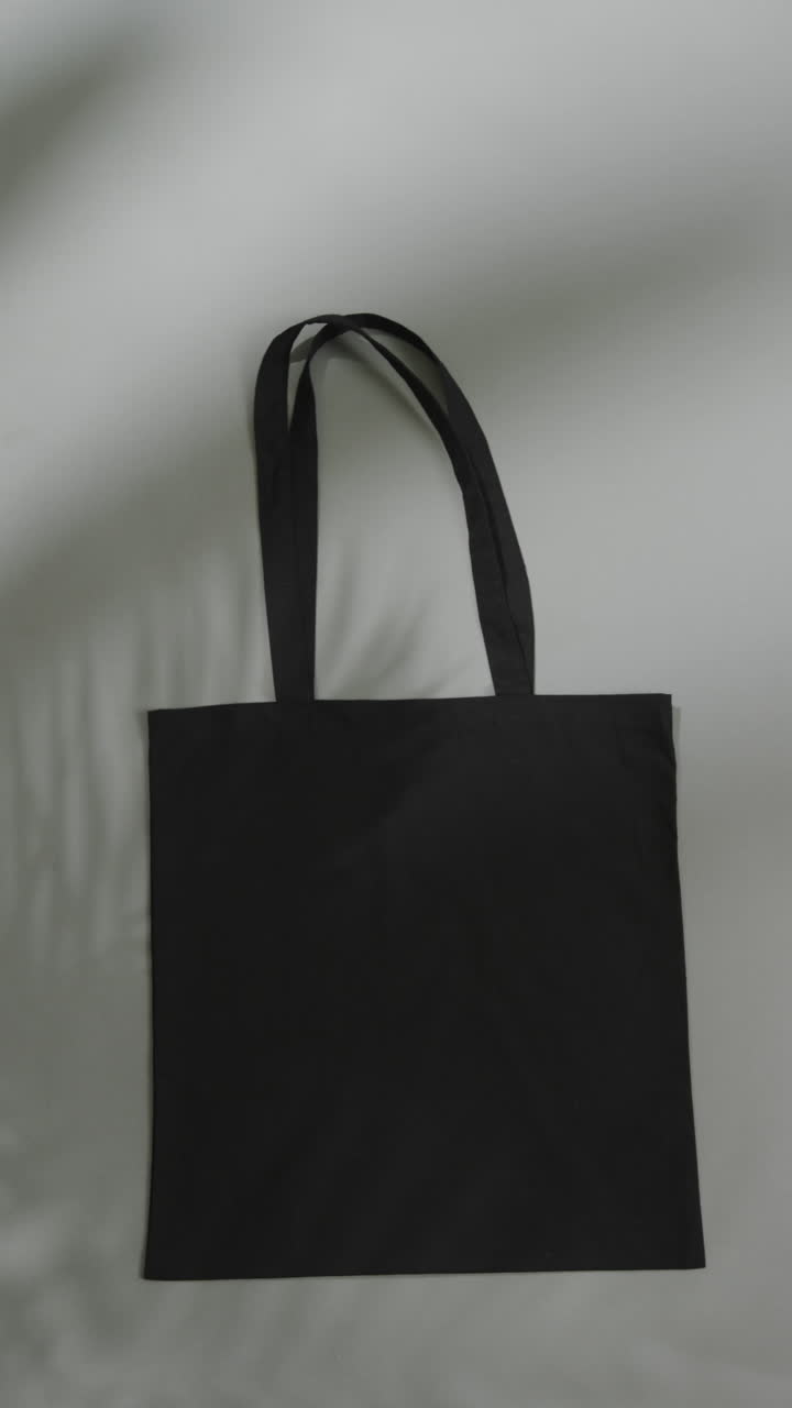 Vertical video of leaf shadow moving over black bag on grey background, copy space, slow motion