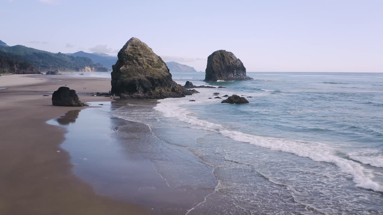 Seastacks at Cannon Beach on the Oregon Coast, Pacific Northwest. Dolly in low angle flight between the rocks reveals the ocean and mountains on the horizon