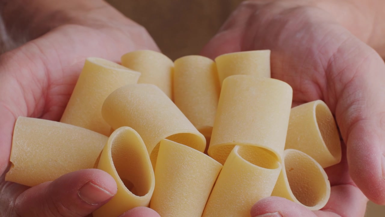 Mani adulte che reggono un mucchio di paccheri italiani secchi e crudi