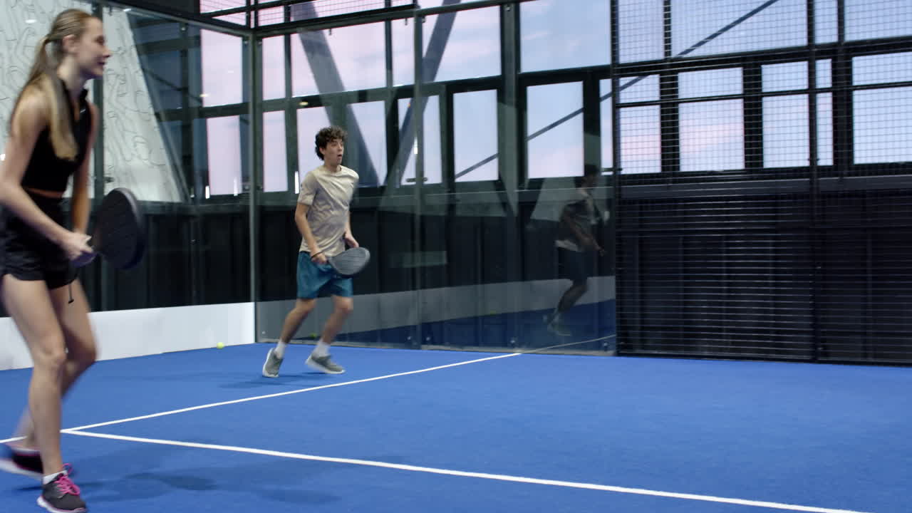 Young man playing padel tennis on blue indoor court, preparing to hit ball