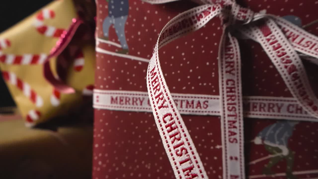 Close up detailed view of colorfully wrapped Christmas presents or gifts with Merry Christmas written on the long ribbon. Candy cane wrapping paper. Black studio background, shallow depth, bokeh