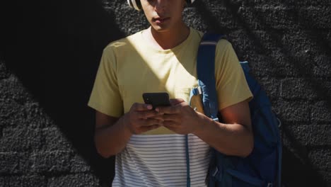 Mid-section-of-mixed-race-man-wearing-headphones-and-using-smartphone-in-the-street