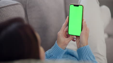 woman sitting on a couch, looking at her phone with a green screen