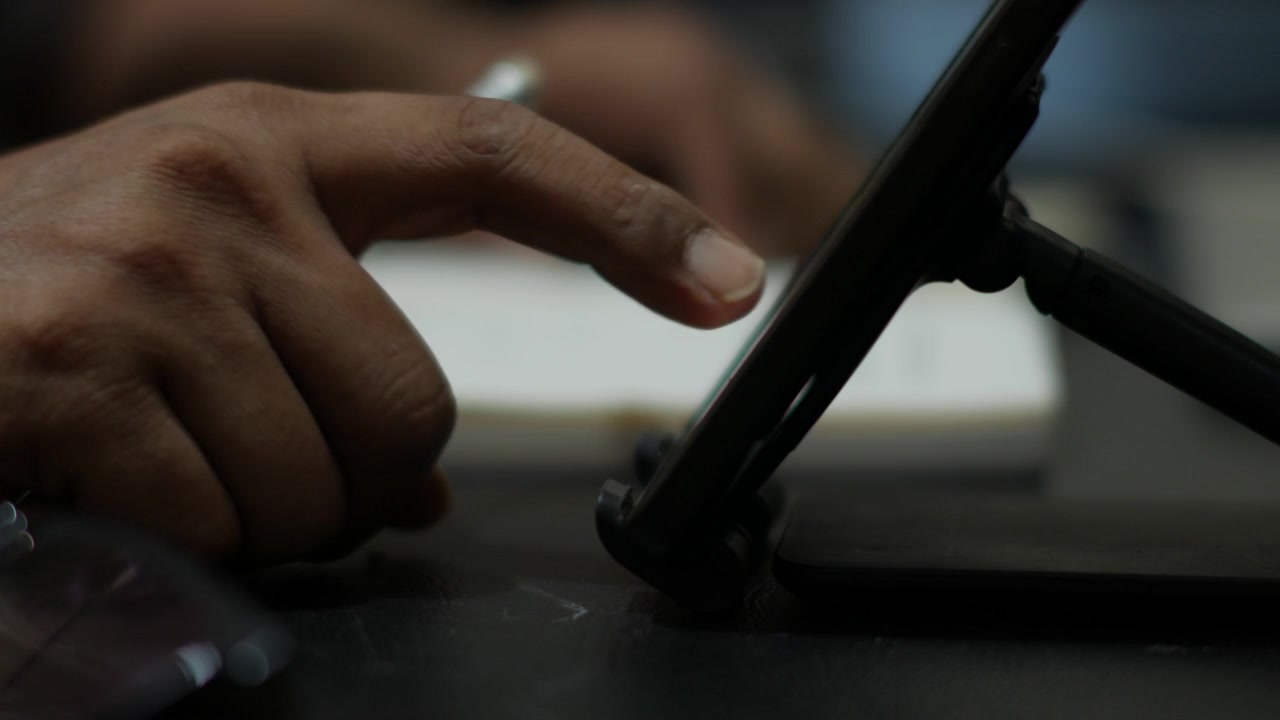 Persona che scrive su un quaderno e scorre lo smartphone alla scrivania