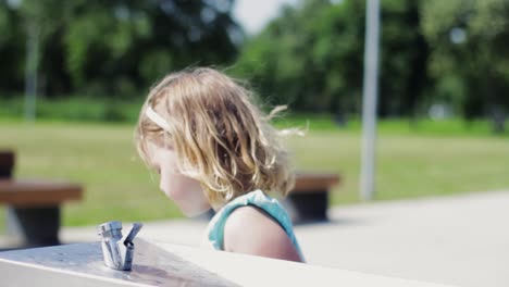 Linda-Niña-Bebiendo-Agua-De-Una-Fuente-De-Agua-Potable-En-Un-Caluroso-Día-De-Verano