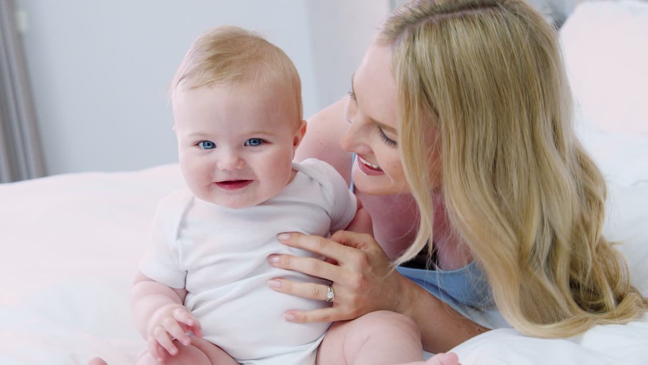 집에서 침대에 누워있는 어머니는 아기 아들에게 키스를줍니다.