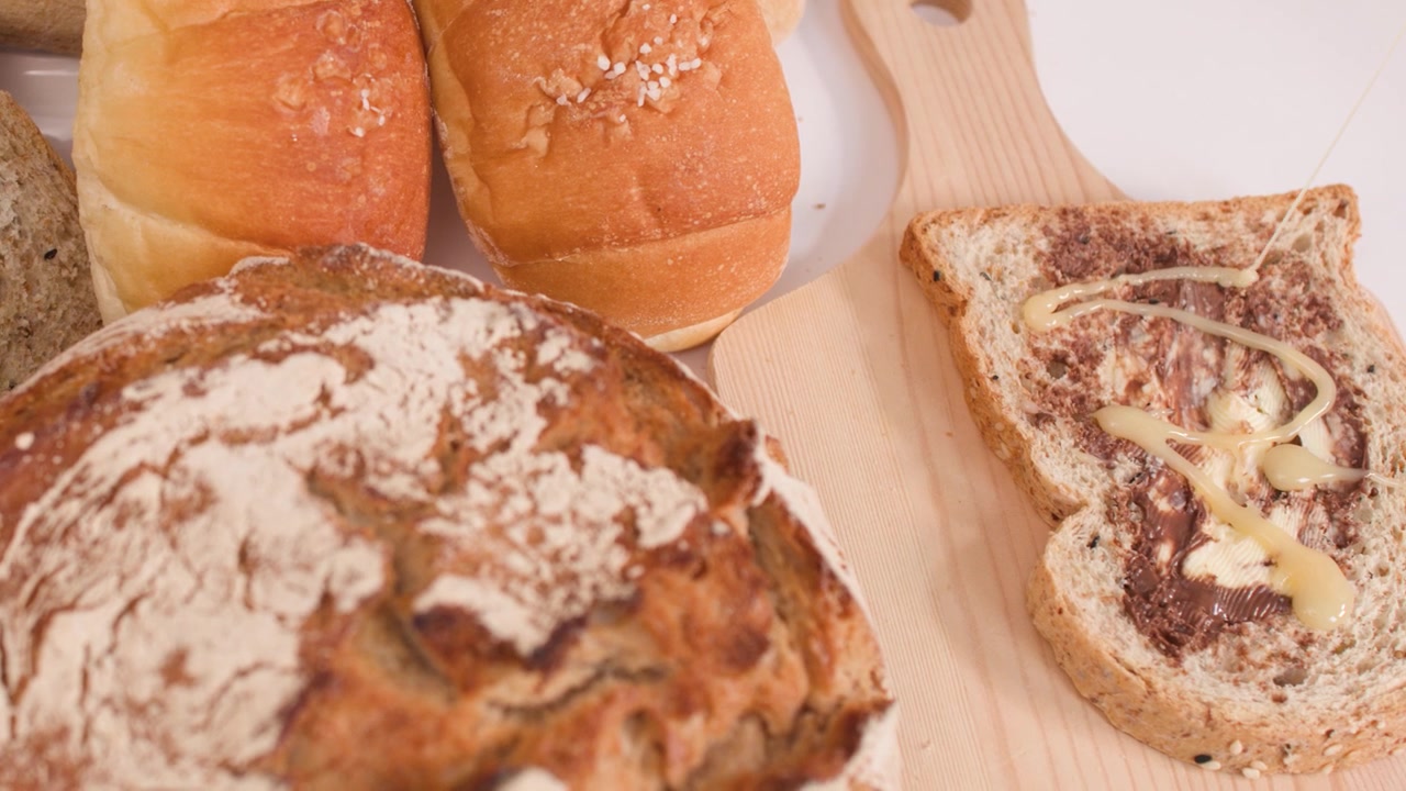 Close-up camera pan across various fresh breads, croissants, and buttered toast on wooden boards.