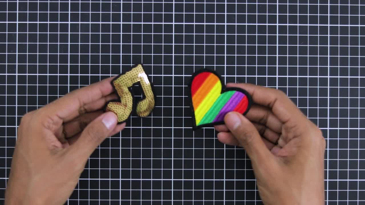 manos sosteniendo nota de música brillante parche y parche de corazón arco iris de colores contra un fondo de cuadrícula