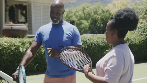 Glückliches-älteres-Afroamerikanisches-Paar-Mit-Tennisschlägern,-Das-Sich-In-Zeitlupe-Auf-Dem-Tennisplatz-Unterhält