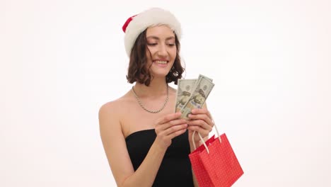 excited woman in santa hat holding money and gift bag for christmas shopping