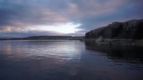 Blue-sunset-over-bay-with-rocky-cliff-and-clouds