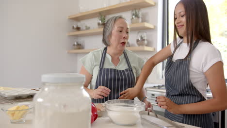 baking together, asian grandmother and granddaughter laughing in kitchen with mixing bowl
