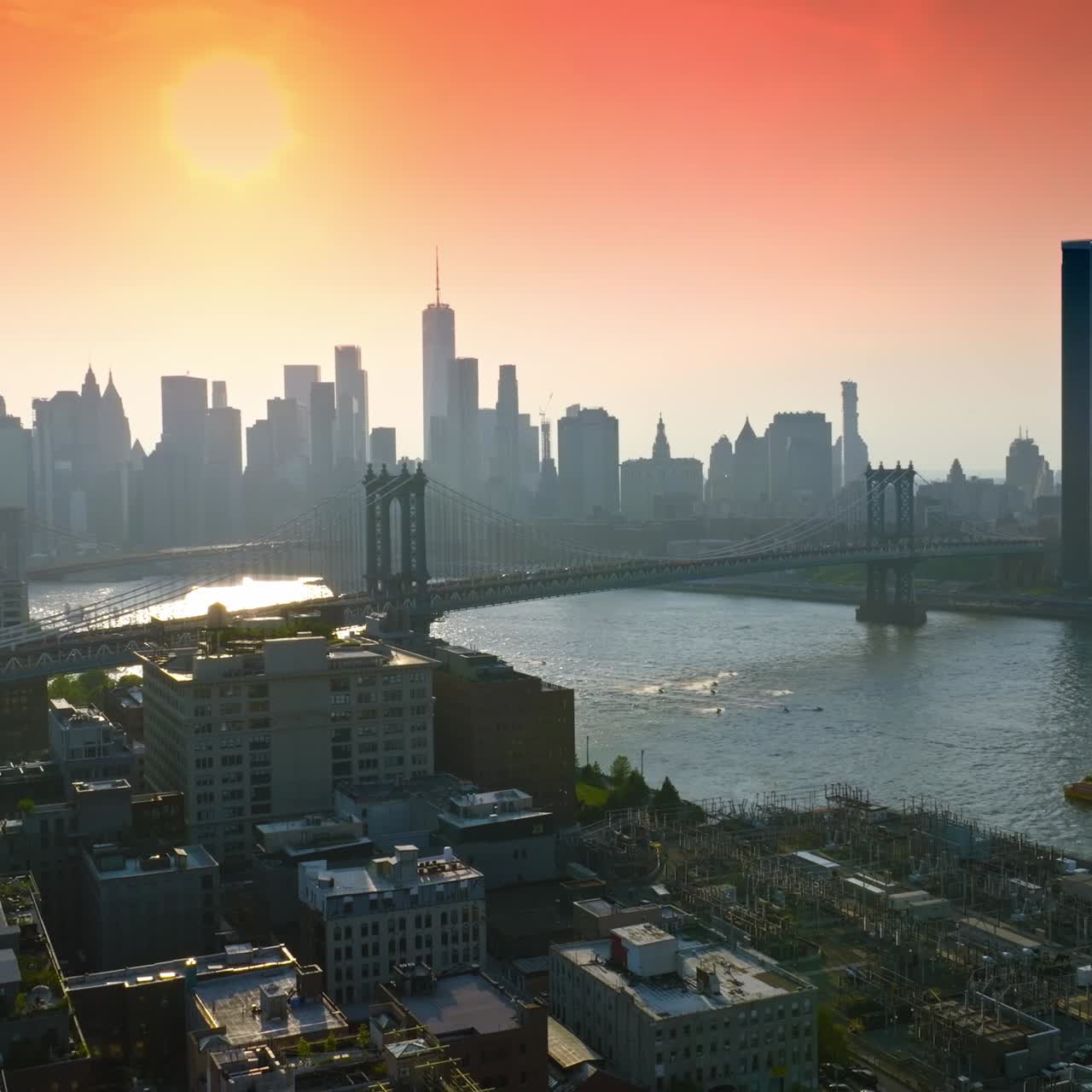 Um belo sol no céu rosa brilhando sobre Nova York. Docas da cidade, Manhattan Bridge sobre o East River e silhuetas de arranha-céus ao fundo