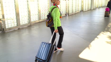 happy, mature woman holding passport and smartphone, rolling luggage through the jetway, to board an airplane