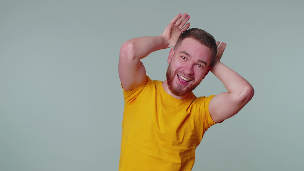 adorabile uomo divertente sorridente amichevole, facendo orecchie di coniglio gesto sulla testa divertendosi ingannando umore comico