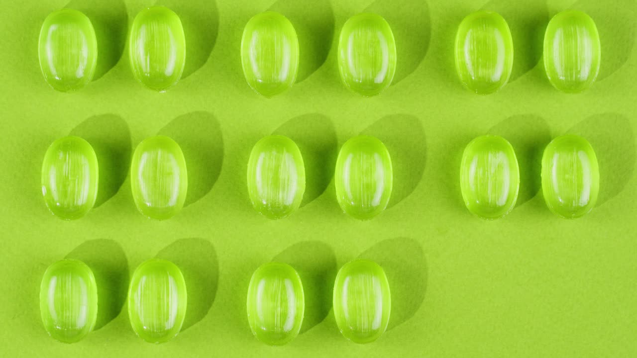 Green mint mentol lollipops, candies, bonbons disappear on purple background. Summer bright texture studio shot for store, supermarket, close up top view. Children favorite sweets made of sugar.