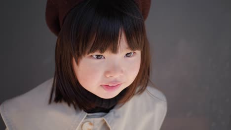 korean girl in a gray coat and cap stands the street in spring at the glass doors of the store