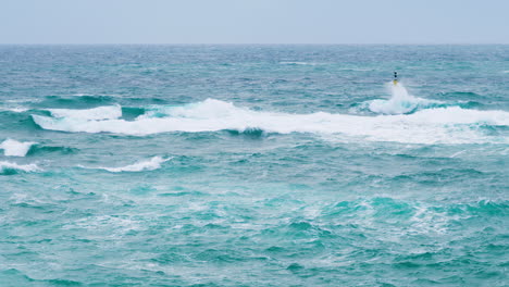 Waves-breaking-on-yellow-cardinal-mark,-stormy-weather-and-restless-sea