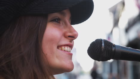 Female-Musician-Busking-Singing-Into-Microphone-Outdoors-In-Street