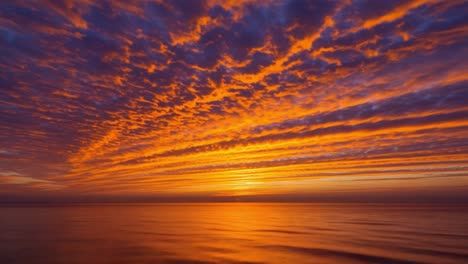 a breathtaking view unfolds as the sun sets over the tranquil ocean. the sky is filled with dramatic clouds painted in shades of orange, pink, and purple, creating a stunning contrast against the deep blue water below. gentle waves ripple across the surface as the sun slowly descends, casting a warm