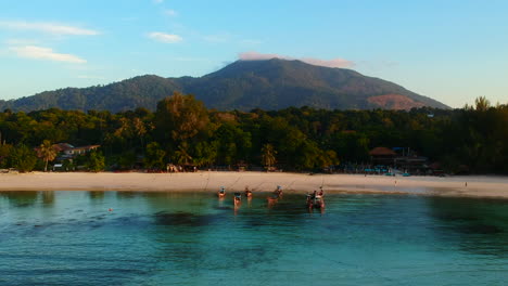 Luftaufnahme-Eines-Weißen-Sandstrandes-An-Der-Küste-Mit-Klarem,-Blauem-Wasser-Und-Einem-Berg-Im-Hintergrund