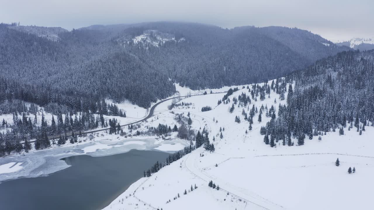 los coches conducen por la ventosa carretera del valle de la montaña en un paisaje helado de nieve invernal, tiro de grúa de drones