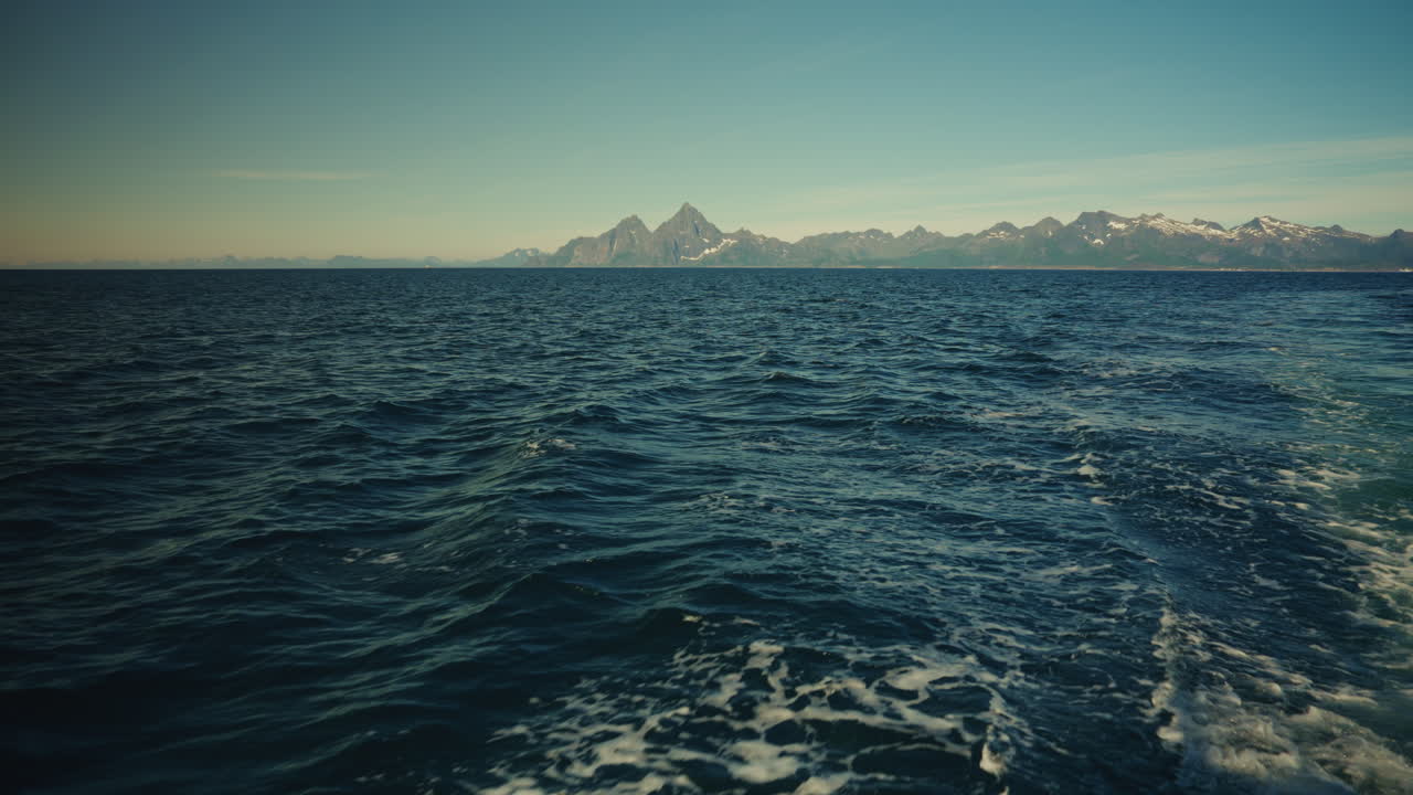 Boat navigating in the Norwegian Sea. View of the Lofoten mountains in the distance, Norway.