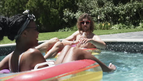 Diverse-couple,-a-young-African-American-woman-and-Caucasian-man,-enjoy-a-sunny-pool-day