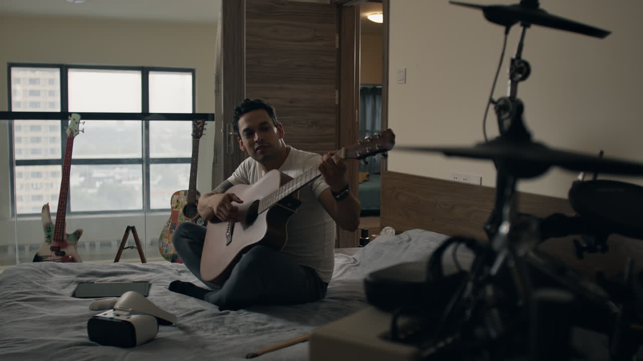 Man plays acoustic guitar seated on bed in music-themed room after removing VR headset