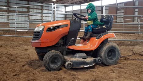 Zweijähriges-Kleinkind-In-Dino-Kostüm-Und-Cowboystiefeln,-Das-Auf-Dem-Rasenmäher-In-Der-Arena-Spielt